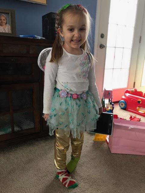Alexandra is wearing crazy clothing for Wacky Wednesday at school.  She has pigtail braids and is wearing a tutu, butterfly wings, and mismatched socks.